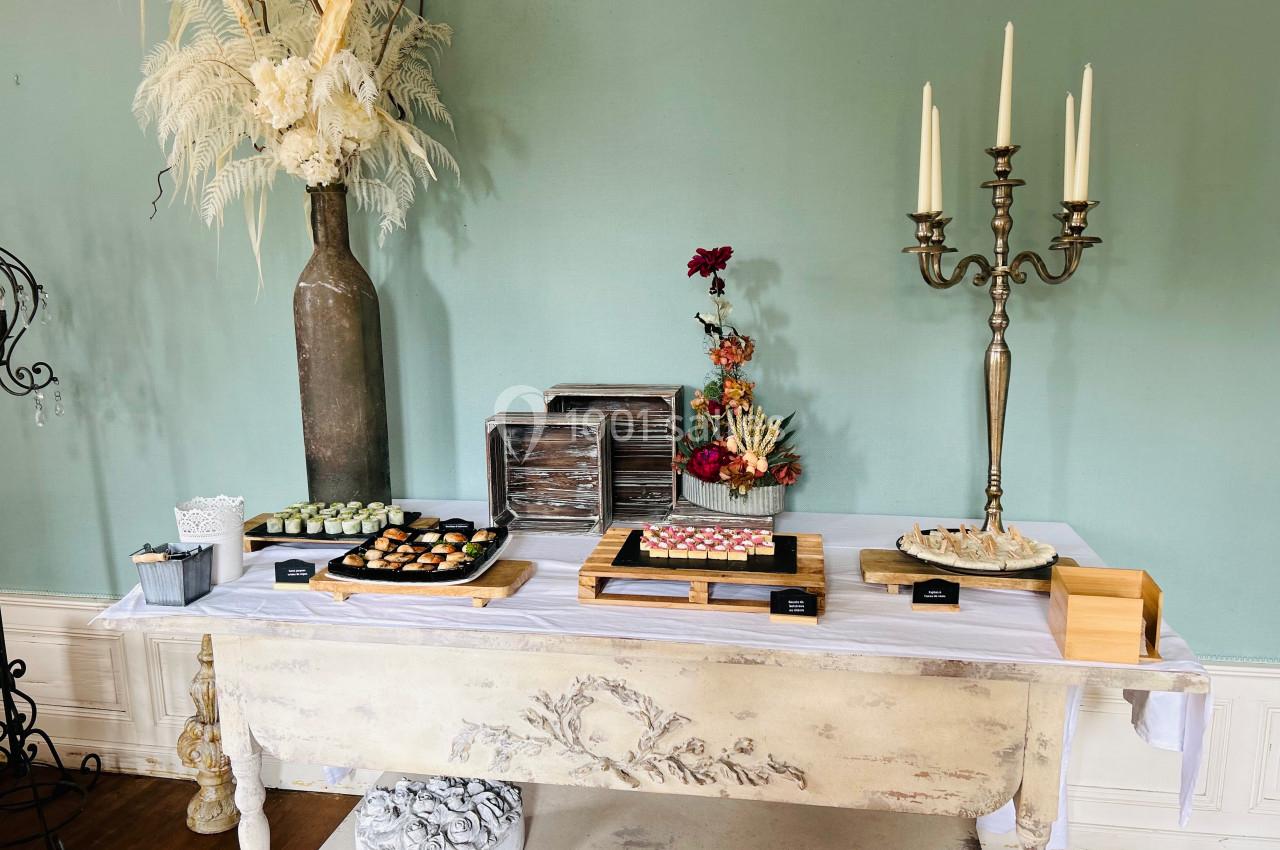 Buffet décoratif avec desserts variés sur une table ancienne, entourée de décorations florales et d'un chandelier.