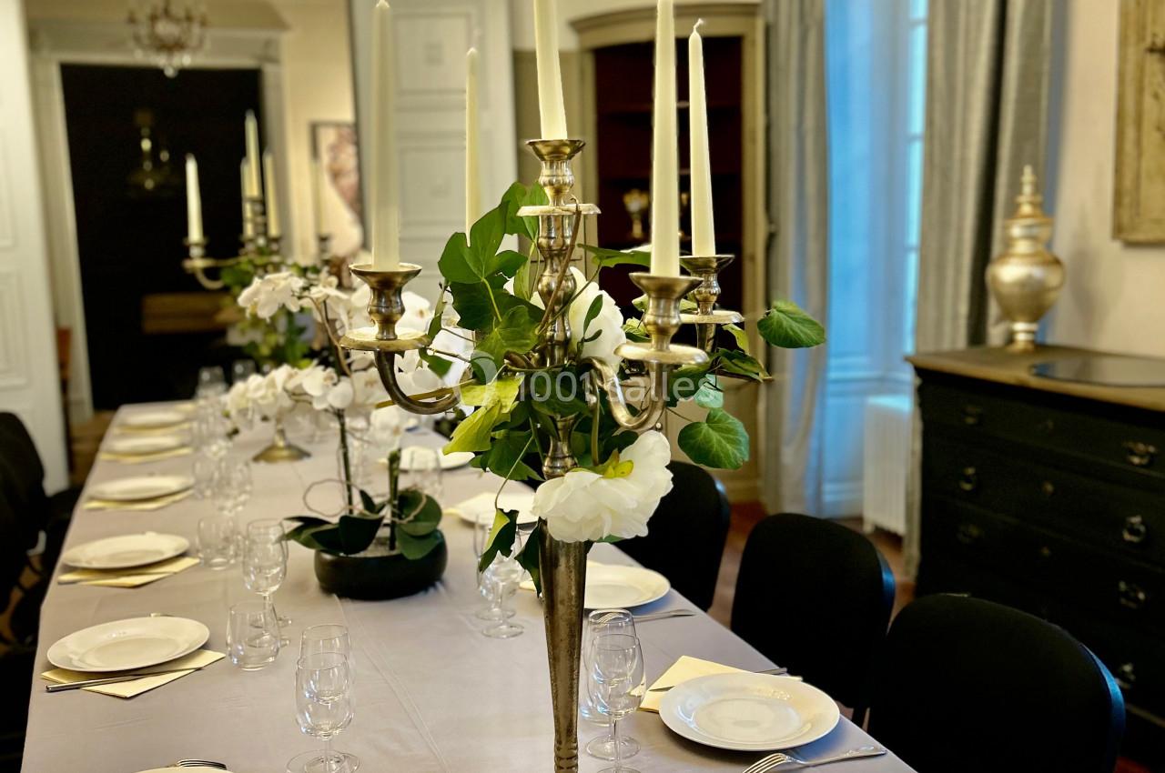 Table élégamment dressée avec chandeliers dorés, vaisselle blanche et décoration florale dans une salle lumineuse.