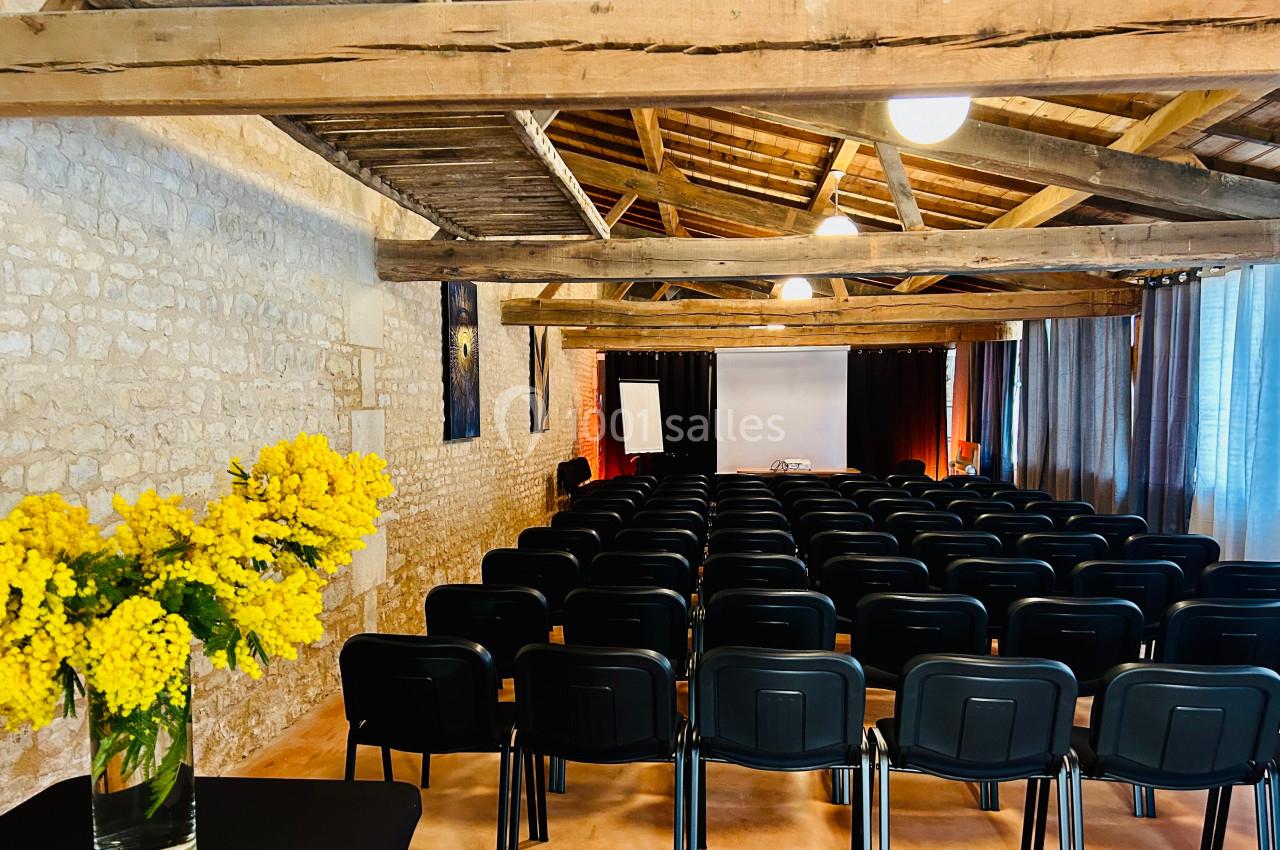Salle de conférence avec des rangées de chaises noires, un écran blanc et un bouquet de fleurs jaunes au premier plan.