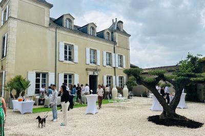 Manoir éclairé de nuit avec des lumières colorées, tables dressées et invités rassemblés dans un jardin.