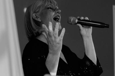 Un homme en costume bleu tient un saxophone sous une pergola décorée de fleurs blanches.