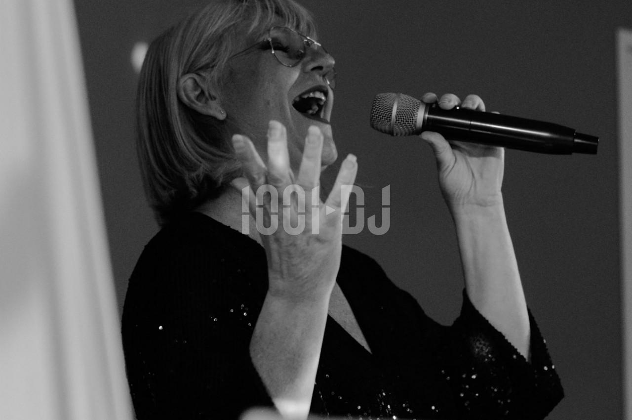 Femme chantant avec un micro à la main, exprimant une émotion intense dans un environnement sombre.