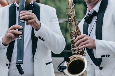 Un homme en costume bleu tient un saxophone sous une pergola décorée de fleurs blanches.