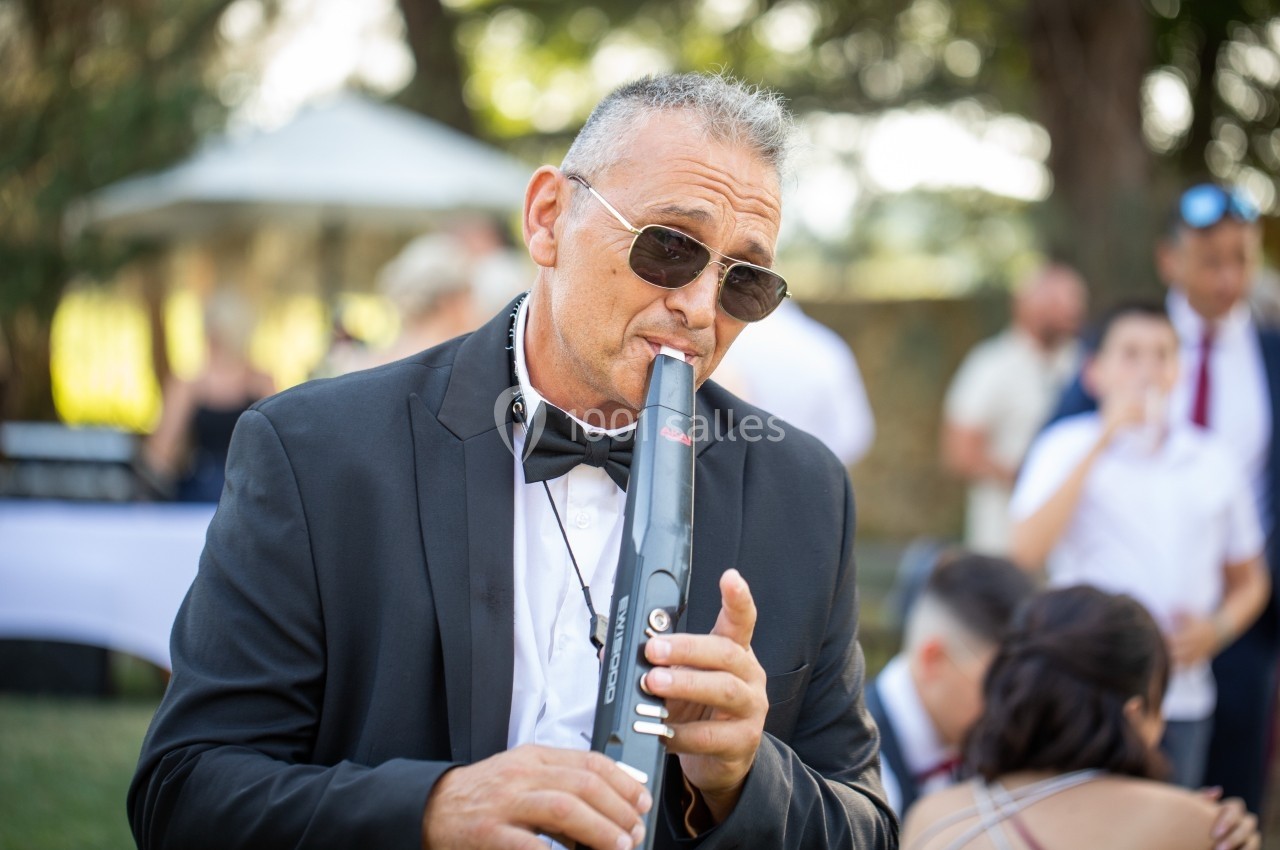 Un homme en costume joue d'un instrument à vent électronique lors d'un événement en plein air.