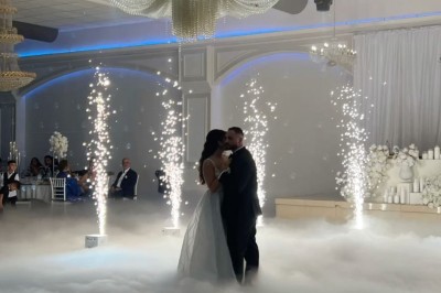 Un homme en costume bleu tient un saxophone sous une pergola décorée de fleurs blanches.