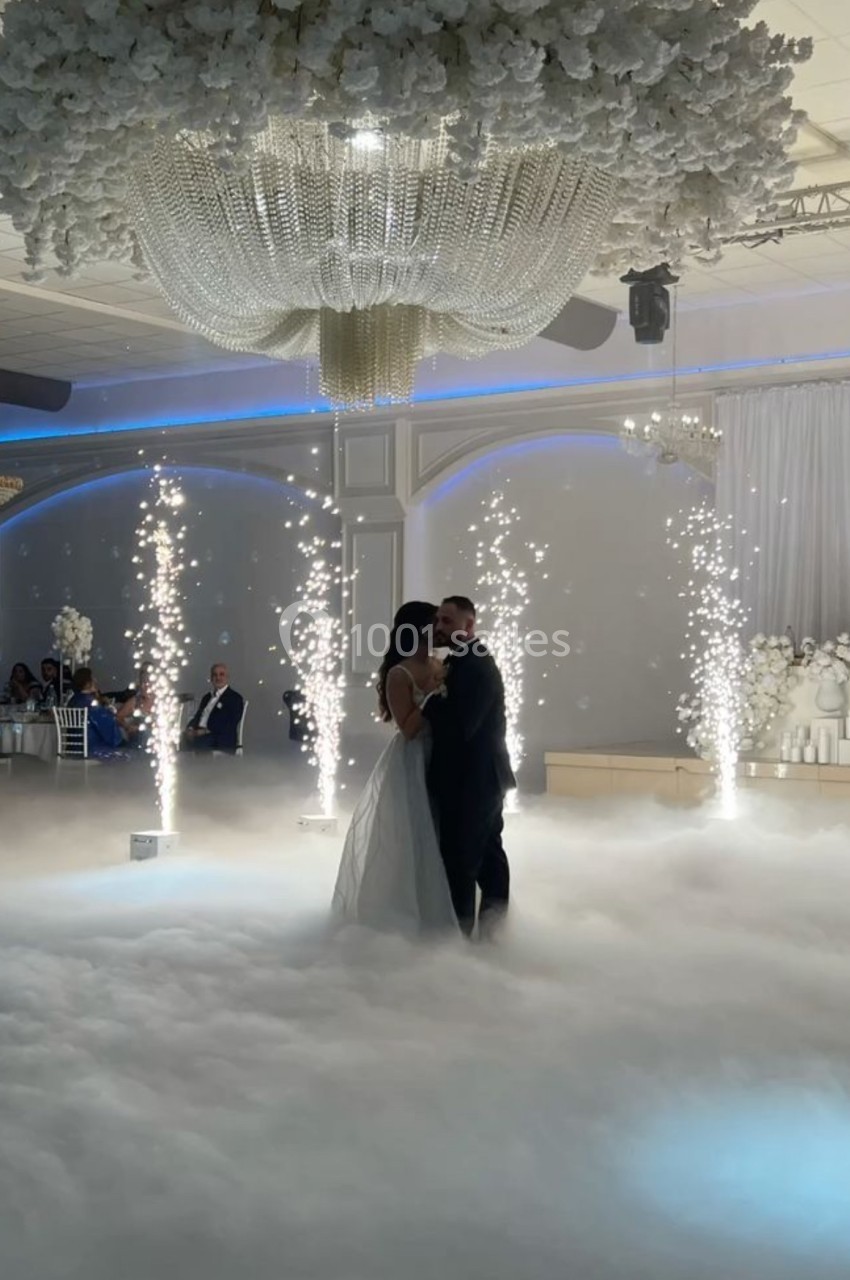 Un couple danse sous un éclairage tamisé, entouré de fumée au sol et de gerbes d'étincelles dans une salle de réception.