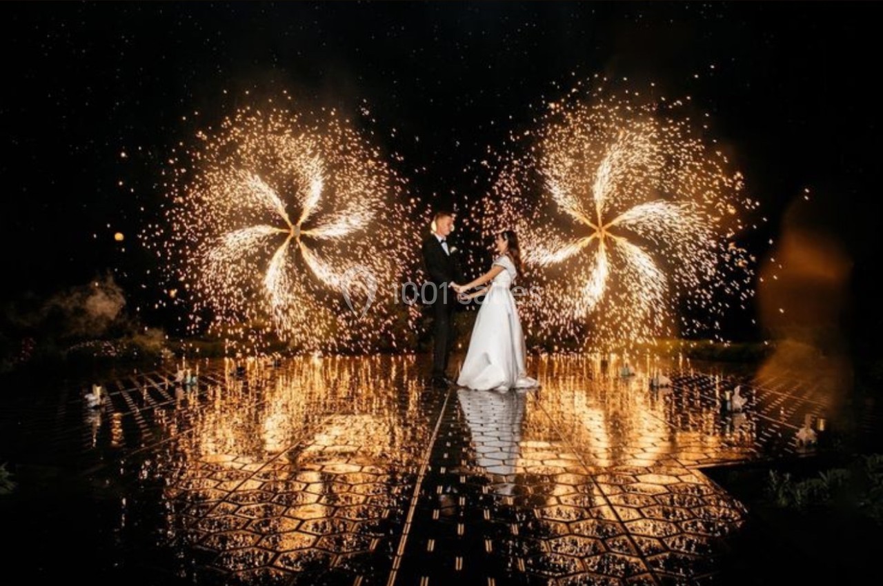 Un couple danse sur une scène réfléchissante entourée de feux d'artifice en spirale dans un décor nocturne.