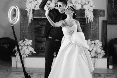 Un homme en costume bleu tient un saxophone sous une pergola décorée de fleurs blanches.