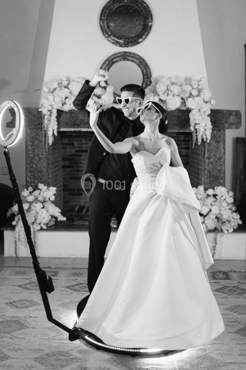 Un couple en tenue de mariage danse avec des lunettes de soleil, entouré de décorations florales et d'un éclairage…