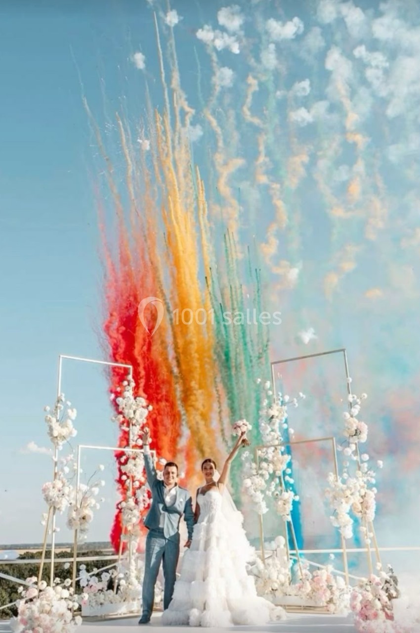 Un couple en tenue de mariage célèbre sous des feux d'artifice colorés, entouré de décorations florales.