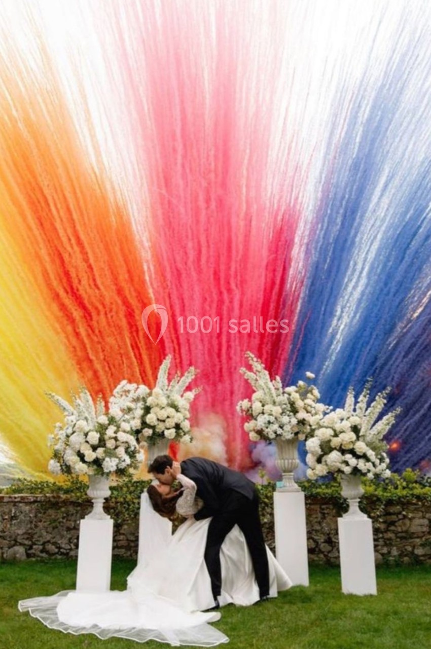 Un couple de mariés s'embrasse devant une explosion de couleurs vives et des arrangements floraux blancs.