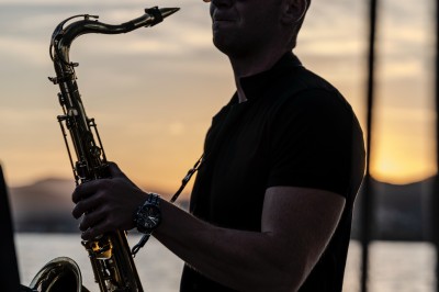Un homme en costume bleu tient un saxophone sous une pergola décorée de fleurs blanches.