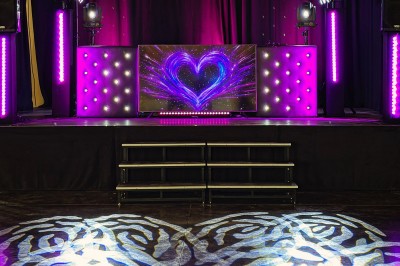Un homme en costume bleu tient un saxophone sous une pergola décorée de fleurs blanches.