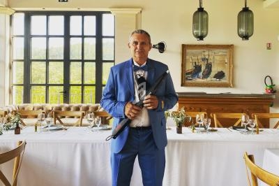 Un homme en costume bleu se tient debout dans une salle lumineuse avec des tables dressées pour un repas.