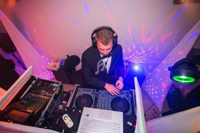 Un DJ mixe de la musique sur une table de mixage, entouré d'équipements et d'effets lumineux colorés.