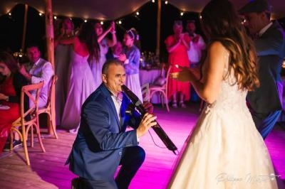 Un homme en costume bleu joue d'un instrument devant une femme en robe de mariée sur une piste éclairée.