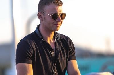 Homme portant des lunettes de soleil et une chemise noire, debout en extérieur sous une lumière naturelle.