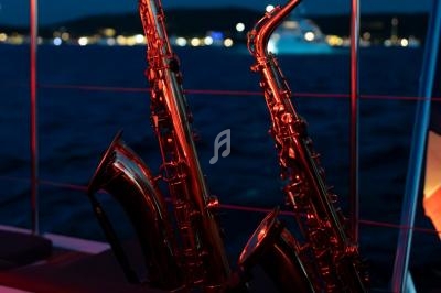 Deux saxophones éclairés par une lumière rouge posés sur un bateau, avec une mer sombre et des lumières au loin.