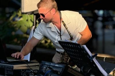 Un musicien jouant du saxophone ajuste un ordinateur portable sur une table équipée de matériel audio.