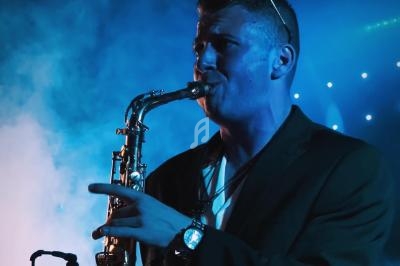 Un musicien joue du saxophone sous un éclairage bleu avec de la fumée en arrière-plan.