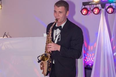 Un musicien en costume joue du saxophone lors d'un événement éclairé par des lumières colorées.