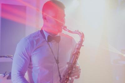 Un homme en costume bleu tient un saxophone dans un intérieur lumineux avec de grandes fenêtres.