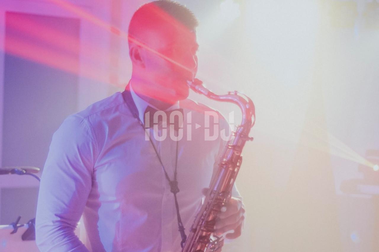 Un musicien en chemise blanche et nœud papillon joue du saxophone sous des lumières colorées.