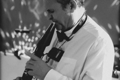 Un homme en costume bleu tient un saxophone dans un intérieur lumineux avec de grandes fenêtres.