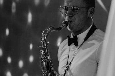 Un homme en costume bleu tient un saxophone dans un intérieur lumineux avec de grandes fenêtres.