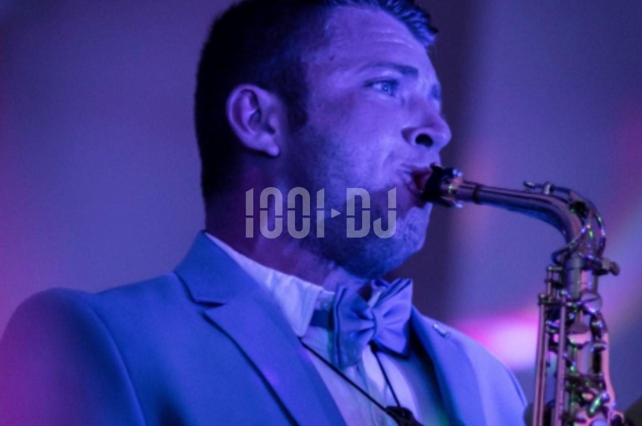 Homme en costume jouant du saxophone sous un éclairage violet.