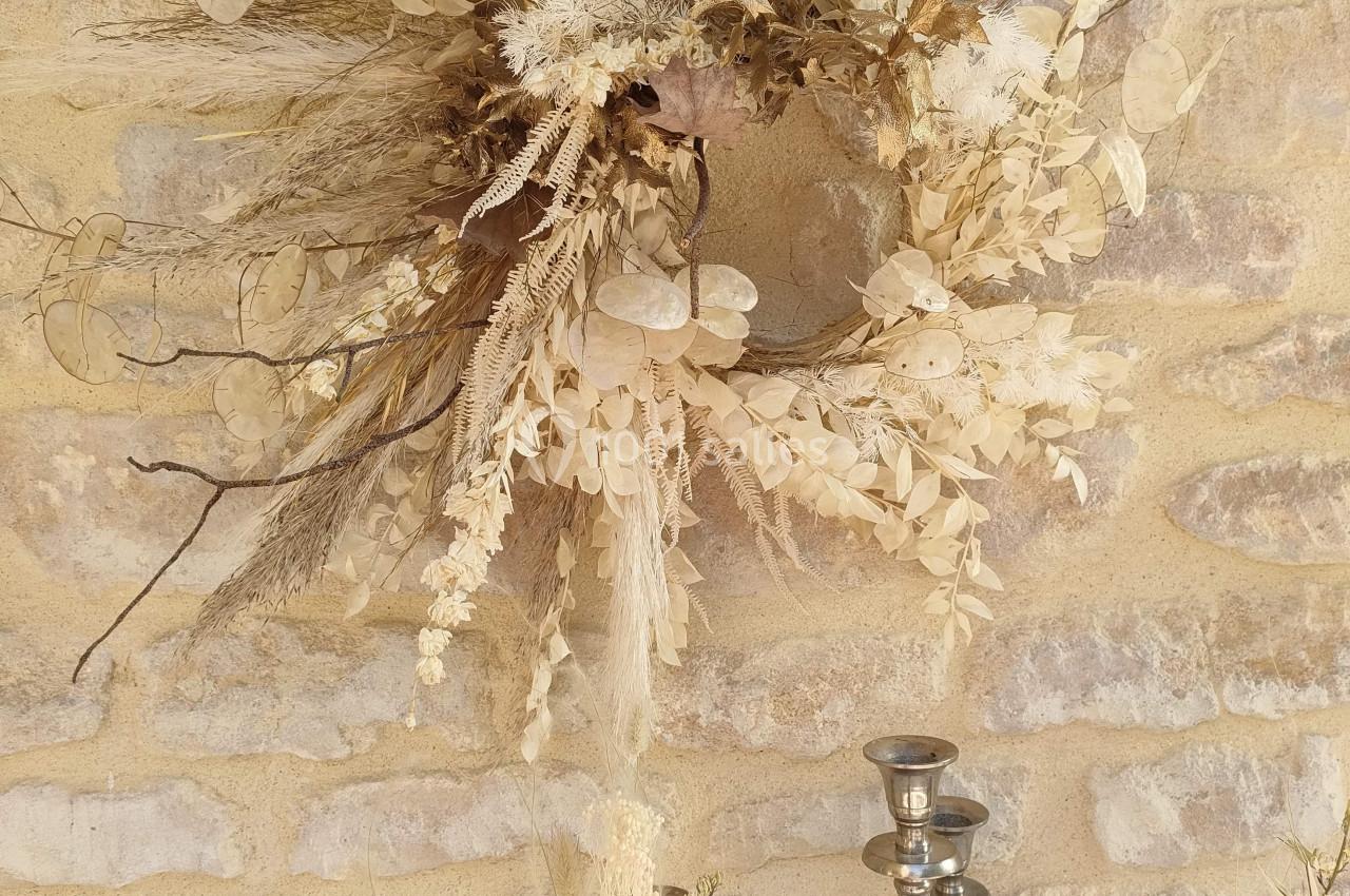 Couronne décorative en fleurs séchées suspendue sur un mur en pierre, avec un chandelier en métal au premier plan.