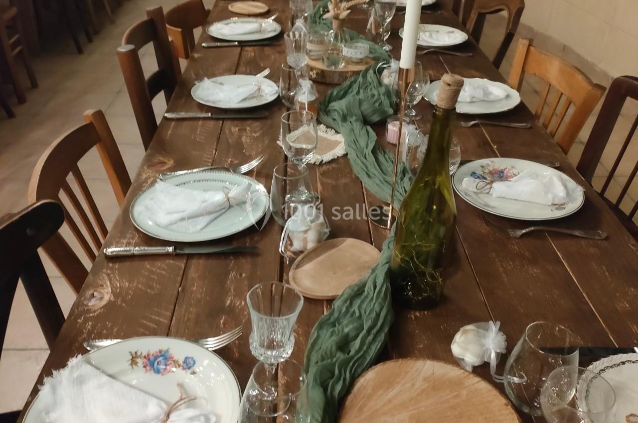 Table en bois rustique dressée pour un repas, avec vaisselle, bougies, rondins décoratifs et chemin de table vert.