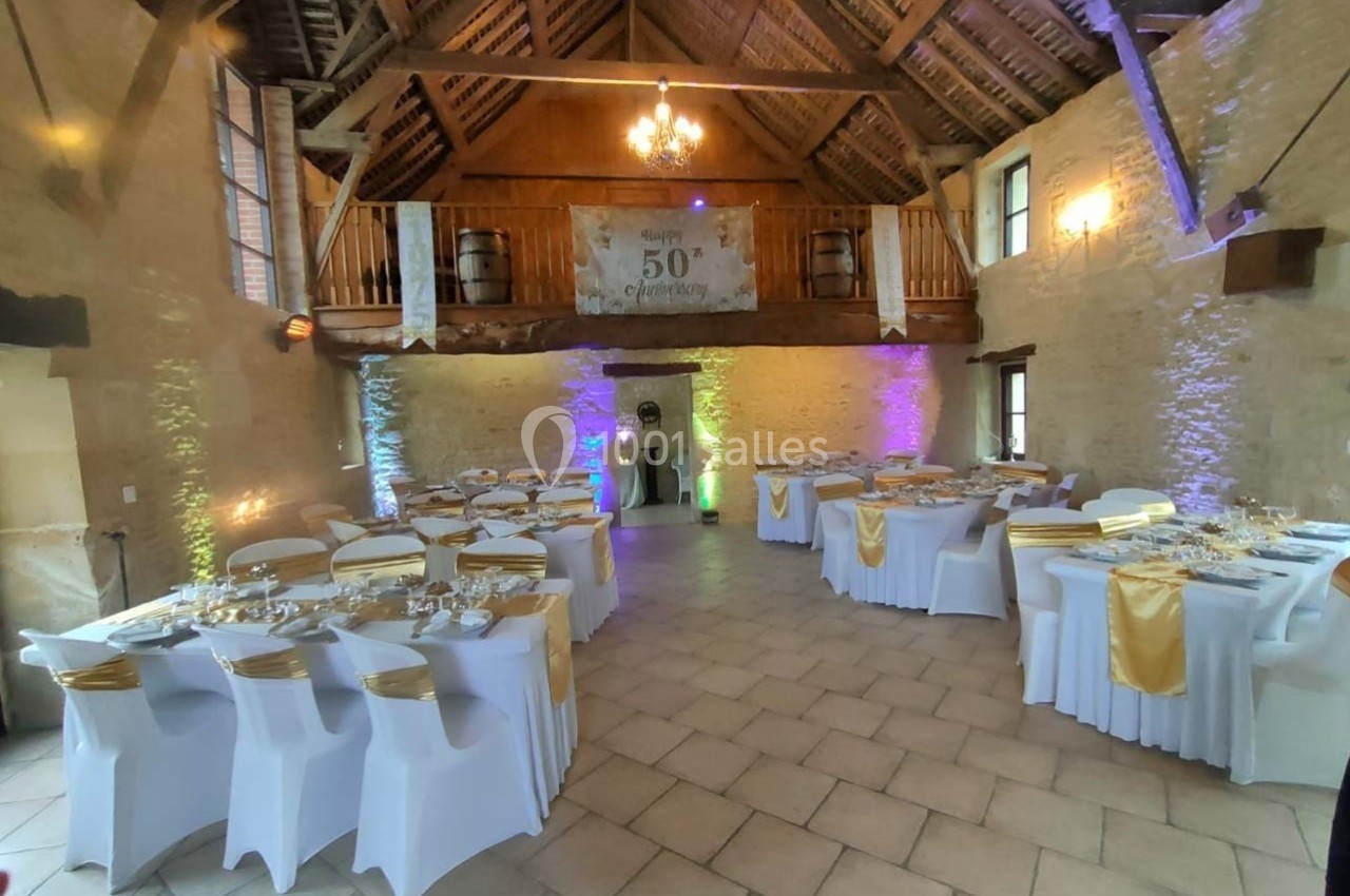 Salle de réception décorée pour un événement, avec tables dressées, nappes blanches et touches de doré.