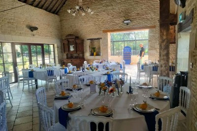 Table en bois rustique dressée pour un repas, avec vaisselle fleurie, bougies, rondins de bois et chemin de table vert.