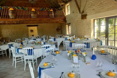 Table en bois rustique dressée pour un repas, avec vaisselle fleurie, bougies, rondins de bois et chemin de table vert.