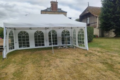 Table en bois rustique dressée pour un repas, avec vaisselle fleurie, bougies, rondins de bois et chemin de table vert.
