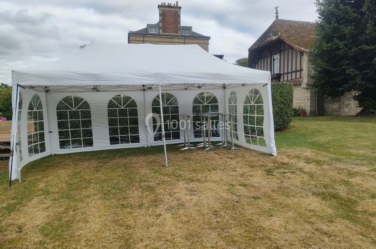 Tente blanche avec fenêtres transparentes installée sur une pelouse, entourée de bâtiments anciens et d'arbres.