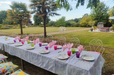 Table en bois rustique dressée pour un repas, avec vaisselle fleurie, bougies, rondins de bois et chemin de table vert.