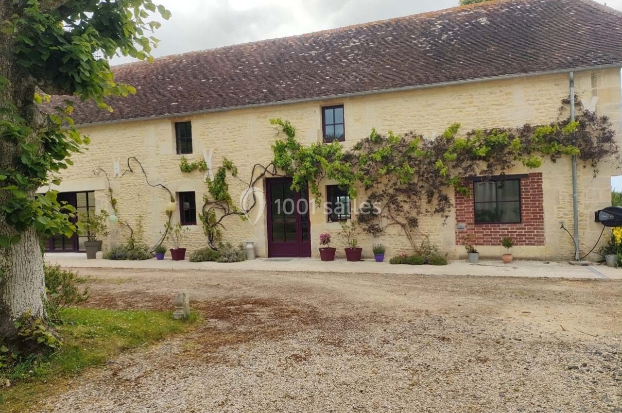 Façade d'une maison en pierre avec des plantes grimpantes, des pots de fleurs et une allée en gravier au premier plan.