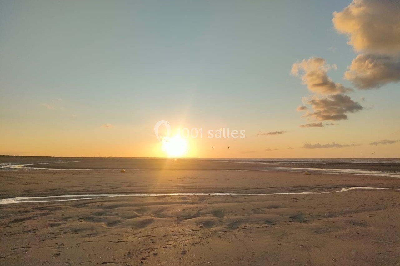 Coucher de soleil sur une plage avec des nuages légers, des reflets sur le sable et des ruisseaux d'eau.