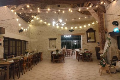 Table en bois rustique dressée pour un repas, avec vaisselle fleurie, bougies, rondins de bois et chemin de table vert.
