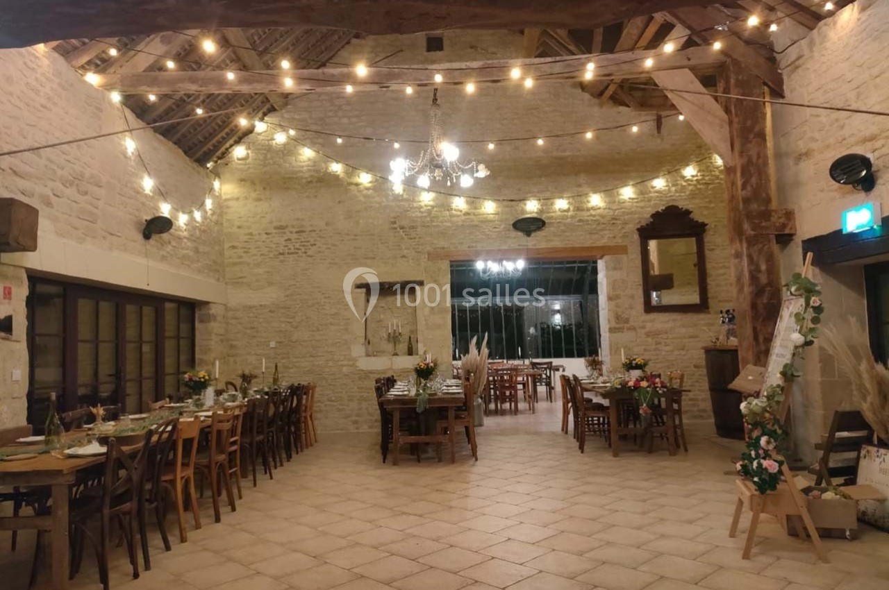 Salle de réception en pierre avec tables dressées, guirlandes lumineuses suspendues et ambiance chaleureuse.