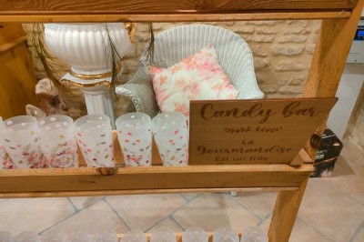 Table en bois rustique dressée pour un repas, avec vaisselle fleurie, bougies, rondins de bois et chemin de table vert.