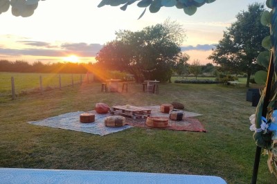 Table en bois rustique dressée pour un repas, avec vaisselle fleurie, bougies, rondins de bois et chemin de table vert.