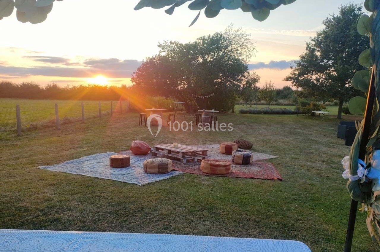 Espace extérieur aménagé avec tapis, coussins et palettes en bois, au coucher du soleil dans un cadre champêtre.