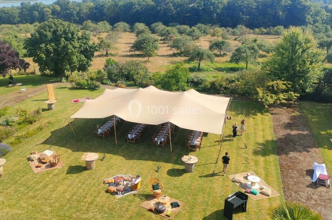 Vue aérienne d'une tente beige installée dans un jardin verdoyant, entourée de tables et de décorations extérieures.