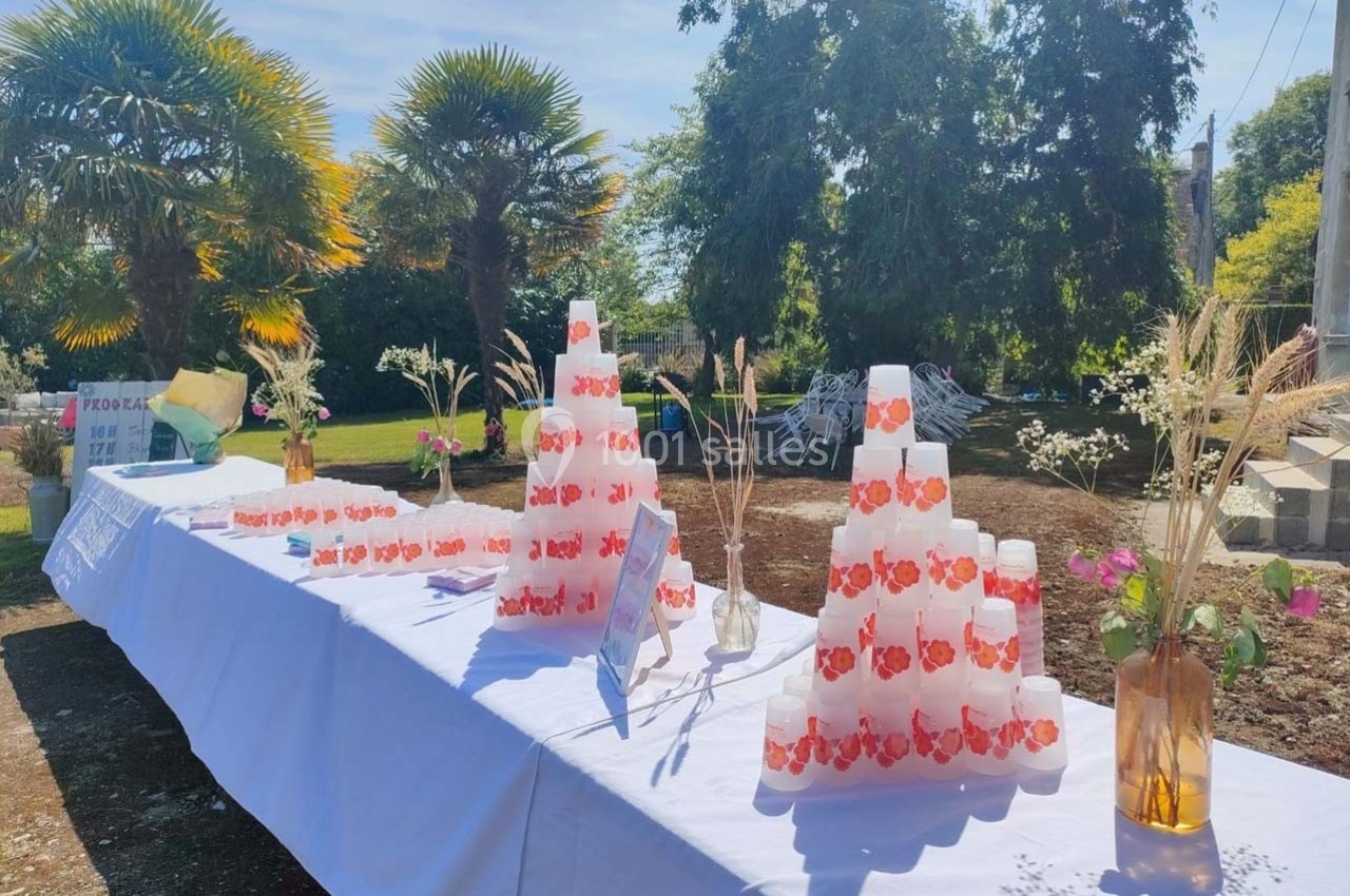 Table dressée en extérieur avec des gobelets empilés, des vases contenant des fleurs et des herbes décoratives.