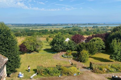 Table en bois rustique dressée pour un repas, avec vaisselle fleurie, bougies, rondins de bois et chemin de table vert.
