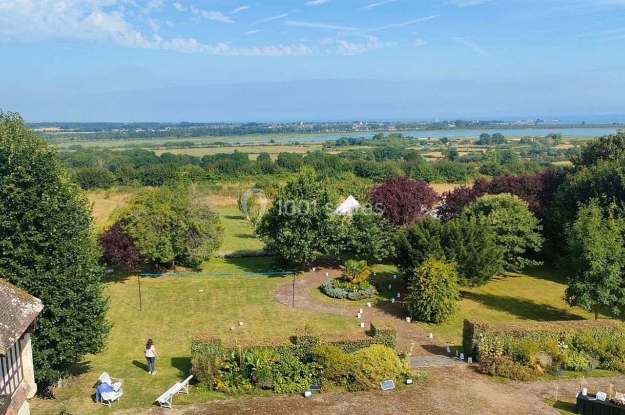 Vue d'un grand jardin verdoyant avec des arbres, des buissons, une pelouse et un paysage côtier en arrière-plan.