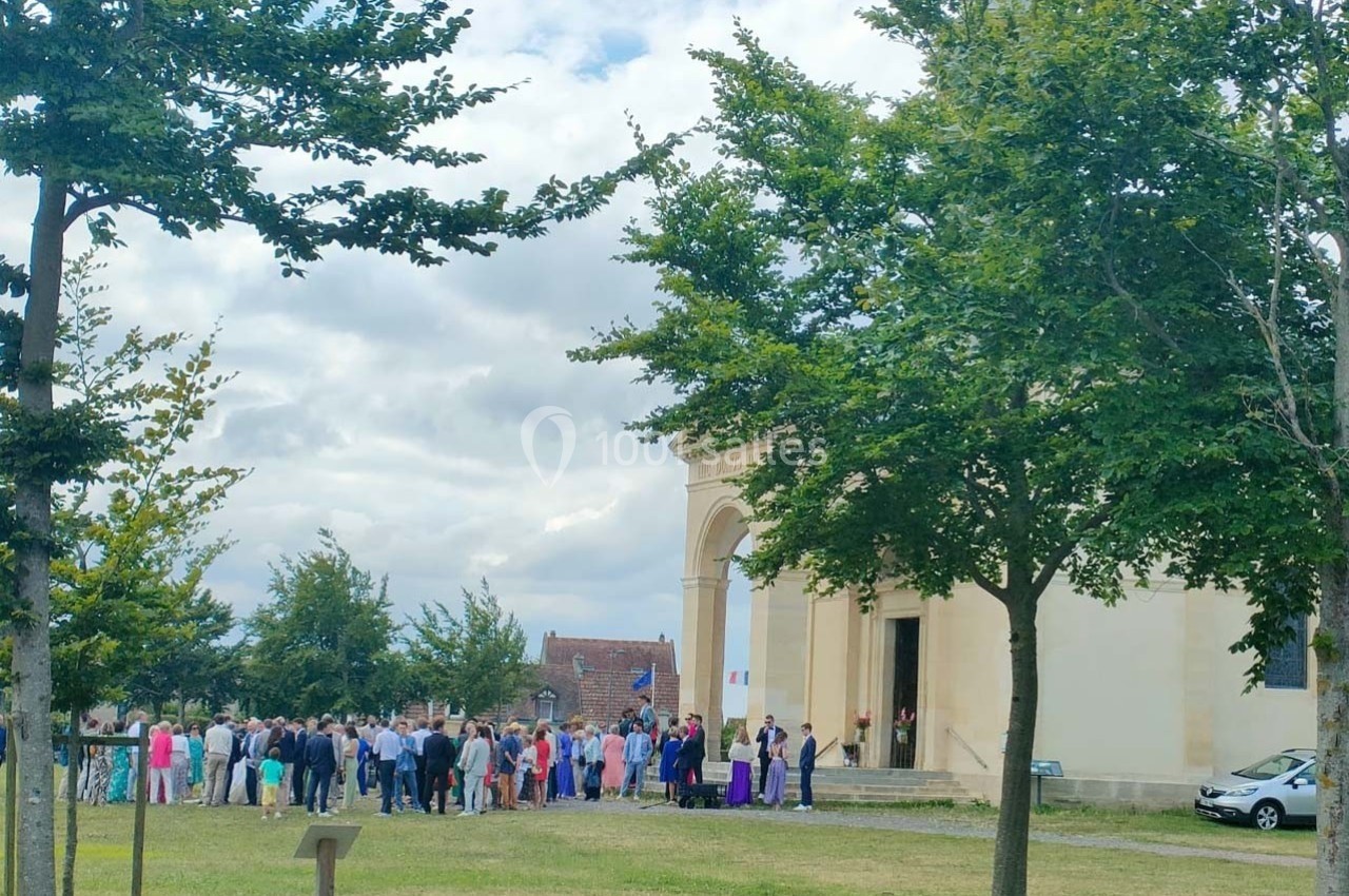 Groupe de personnes rassemblées devant un bâtiment beige avec des arbres et un ciel partiellement nuageux.